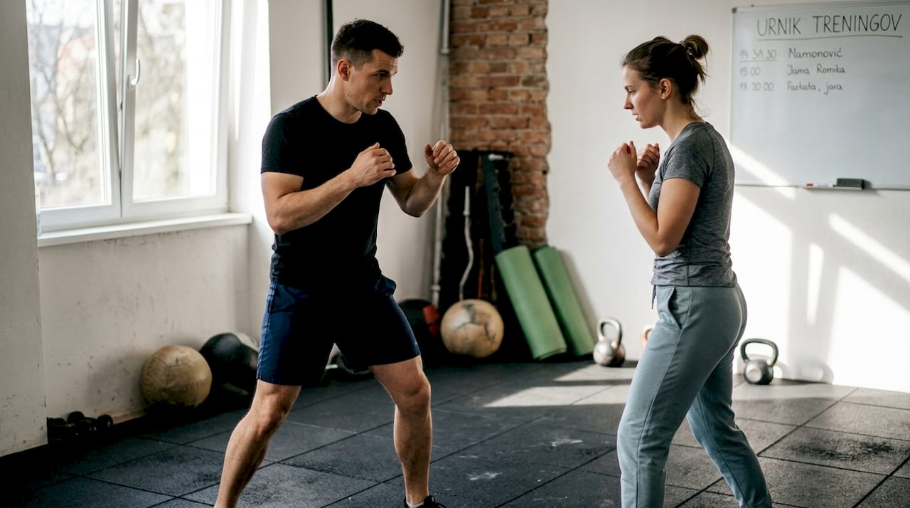 Osebni trener v fitnesu pomaga pri učenju pravilne boksaške drže.